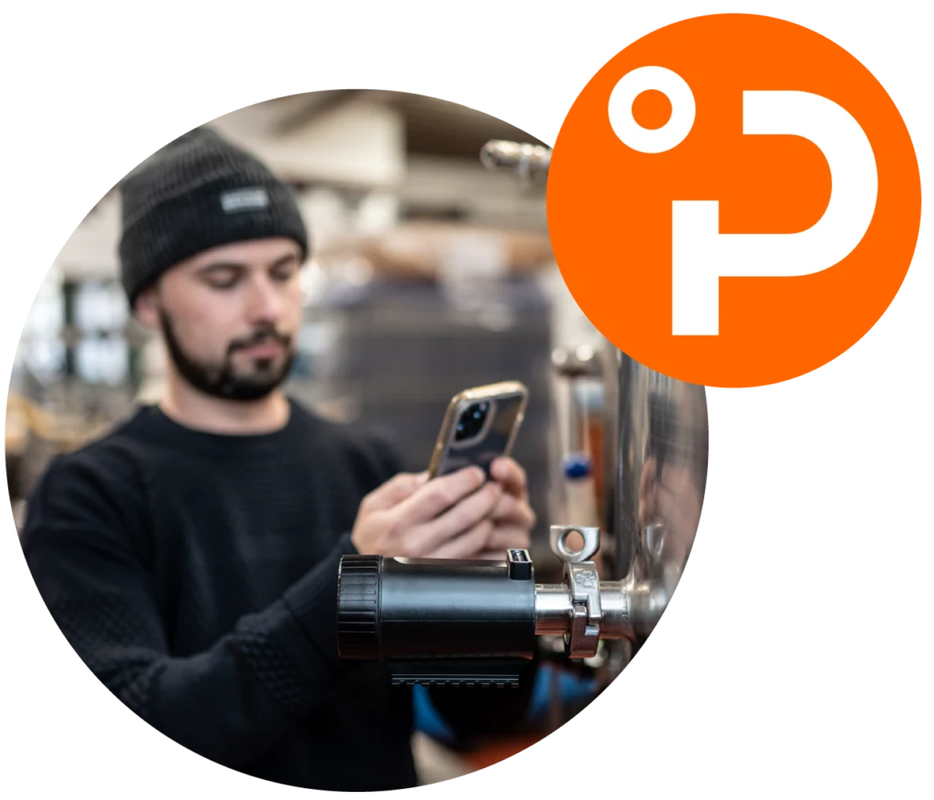 Mann überwacht Brauprozess mit PLAATO Sensor und Smartphone. Im Eck des Bildes hängt ein oranger Kreis mit weißem PLAATO-Signet.