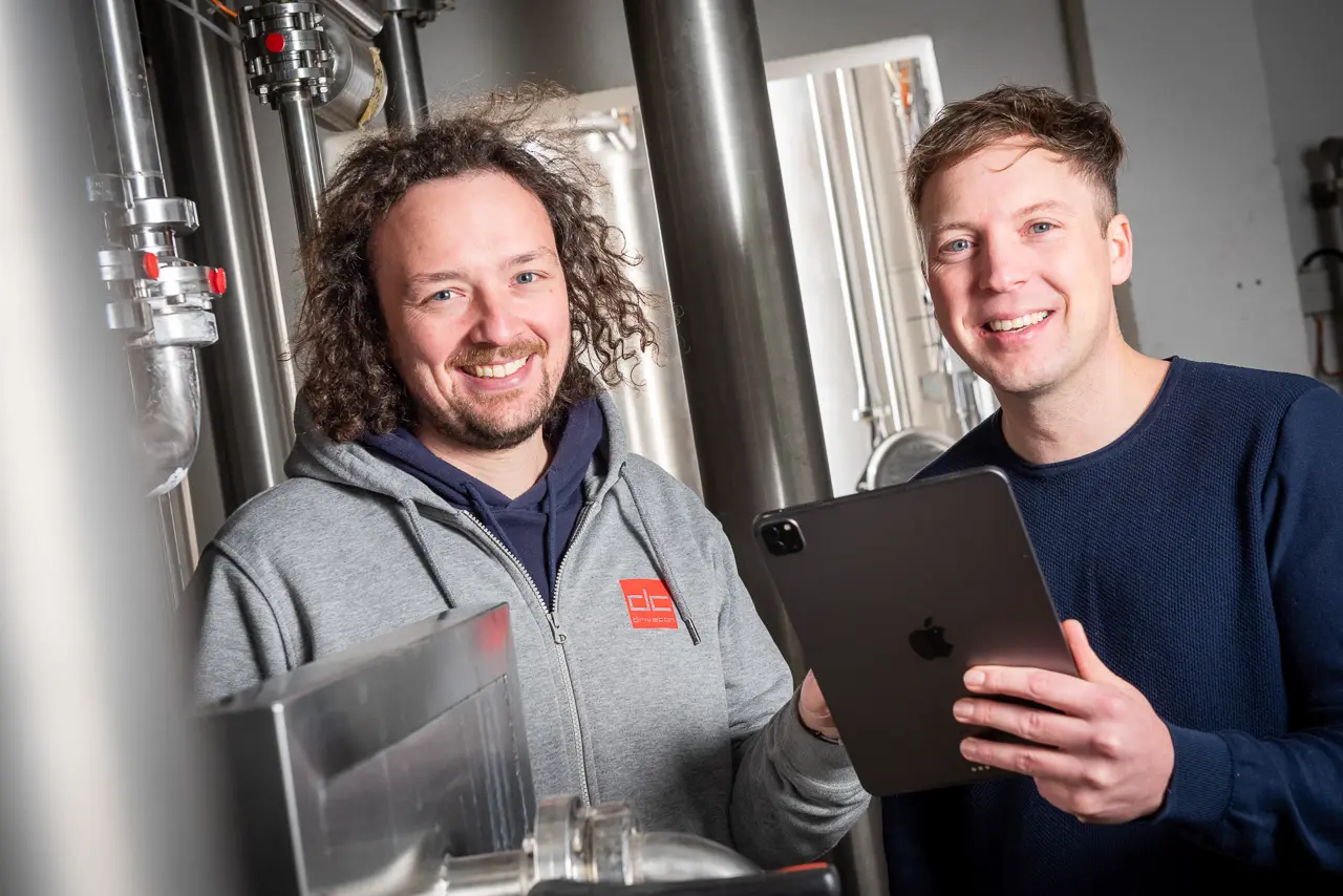 Andreas (links) und Michael (rechts) Weisenseel stehen mit einem Tablet in einer Brauerei und überprüfen die Anlage mithilfe von MINGLECONTROL